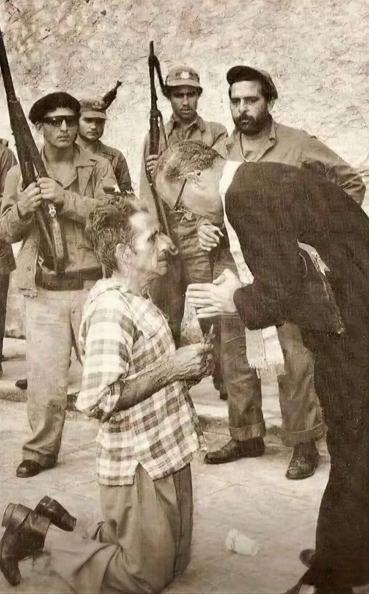 A man kneeling with a crucifix while a priest leans toward him and armed guards with bayonets stand behind