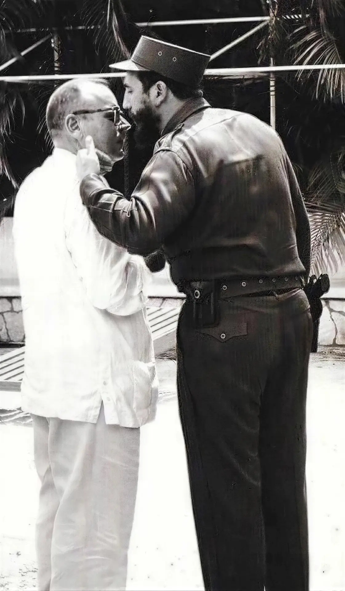 Fidel Castro in uniform and cap touching the face of a man in white with glasses