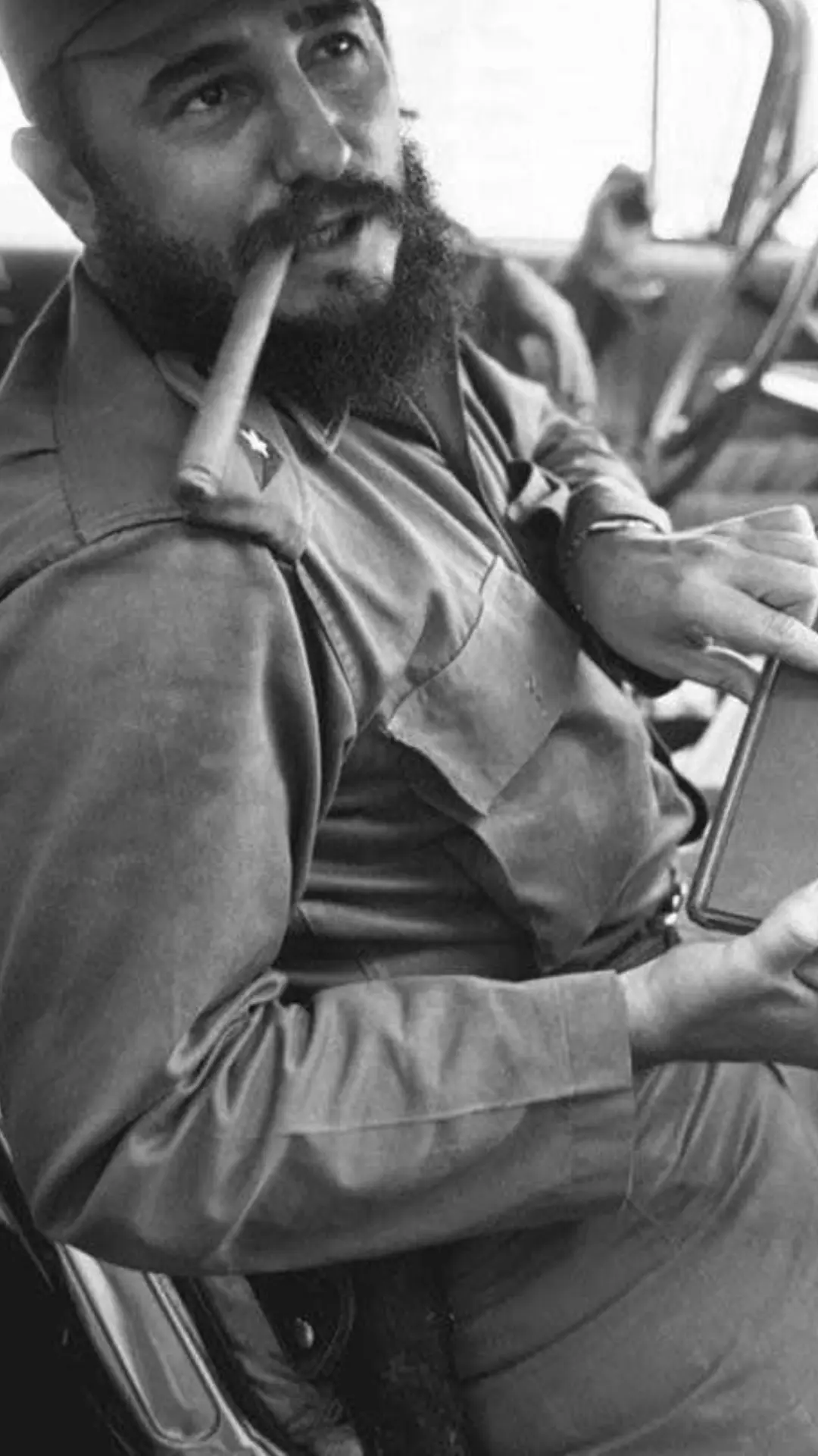 Black-and-white photograph of Fidel Castro in uniform with a cigar, seated in a vehicle