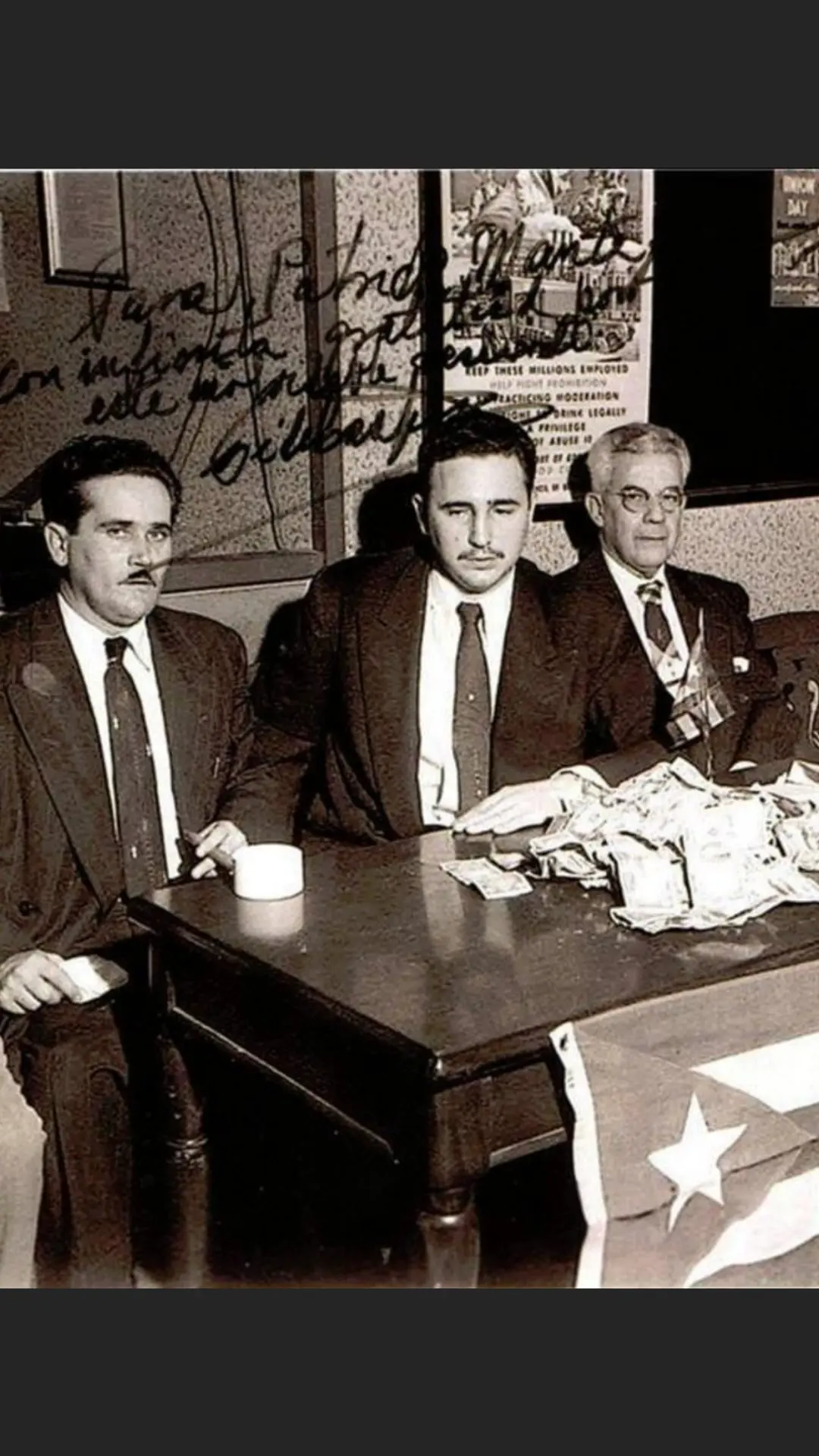 Fidel Castro seated at a desk with a pile of banknotes and a Cuban flag, a handwritten dedication across the top