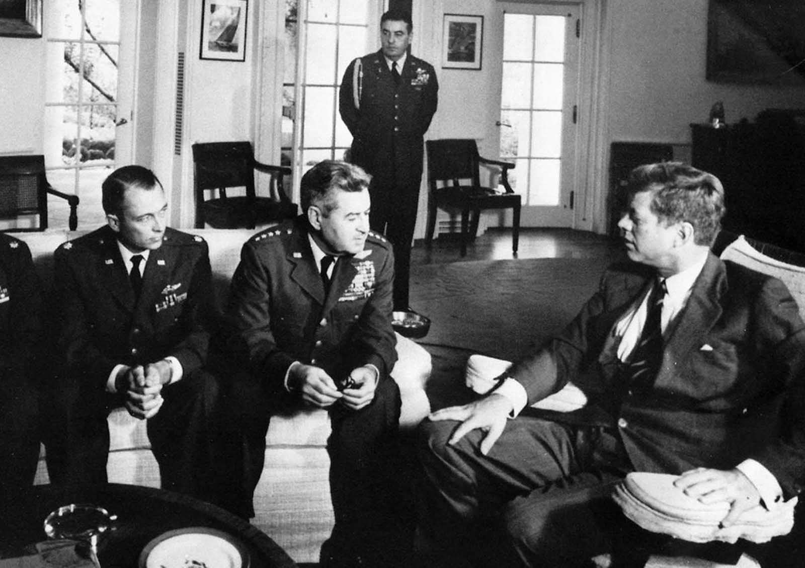 President Kennedy seated in conversation with uniformed Air Force officers in the Oval Office