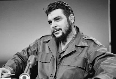 Black-and-white portrait of Che Guevara in fatigues seated before a microphone