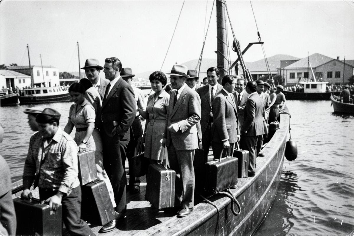 Families with suitcases boarding a boat in a crowded harbor